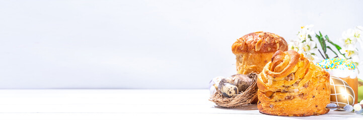 Easter baking background with traditional holiday cakes - kraffin, panettone, paska kulich, with Easter eggs, spring flowers on white wooden table, spring holiday Easter greeting card background