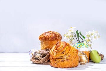 Easter baking background with traditional holiday cakes - kraffin, panettone, paska kulich, with Easter eggs, spring flowers on white wooden table, spring holiday Easter greeting card background