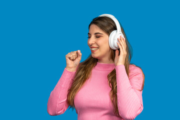 Young woman enjoying music with wireless headphones on blue background