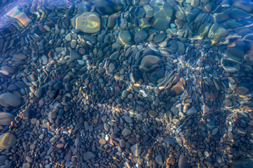 Underwater pebble backgrounds. Colorful stones sea bottom in the sun rays. View from above through clear water. Seascape wallpaper texture. Defocus.