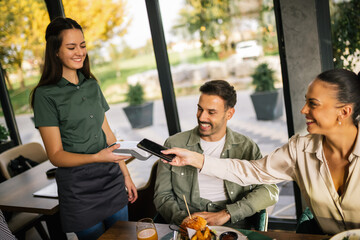 Customers paying for their meal at a restaurant using their mobile phone, utilizing digital payment technology