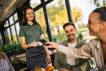 Customers paying for their meal at a restaurant using their mobile phone, utilizing digital payment technology