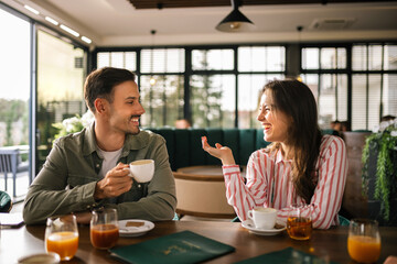 Young couple sitting together in a cozy café, enjoying coffee and engaging in a warm conversation.