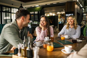 Group of young people sitting at a table in a modern café, enjoying their time together with cups of coffee and glasses of freshly squeezed juice.