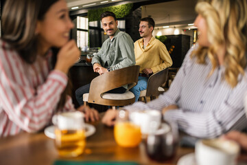 Group of female friends drinking coffee at the restaurant while the guys in the back try to flirt and send them drinks.
