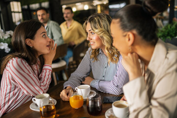 Group of female friends drinking coffee at the restaurant while the guys in the back try to flirt and send them drinks.