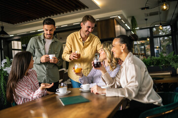 Two young men approaching a group of women at a café, engaging in friendly conversation