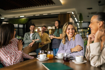 Group of female friends drinking coffee at the restaurant while the guys in the back try to flirt and send them drinks.