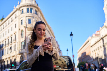 Fototapeta premium Young Caucasian woman using smartphone in front of historic building