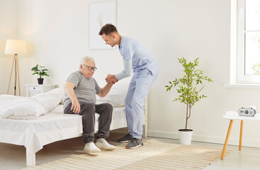 Caring male doctor or nurse helping a senior patient get out of bed after wake up in the morning at a nursing home. Compassionate healthcare, morning routines, and essential assistance.