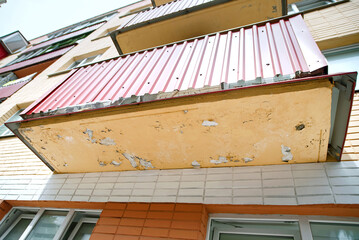 Damaged balcony with cracked plaster and peeling paint on exterior wall of residential building. Structural decay on an old apartment balcony with visible cracks and peeling paint, weathering effects