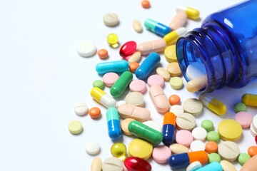 Various pills pouring out of medicine bottle on white background