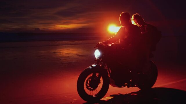 Man and woman ride motorcycle along the ocean in Bali with red signal fire or a rocket. Couple sitting or riding on a scooter on beach, sunset. Concept of friendship, love. Adventures on road trip