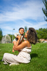 Happy afro mother lifting and playing with baby in green park