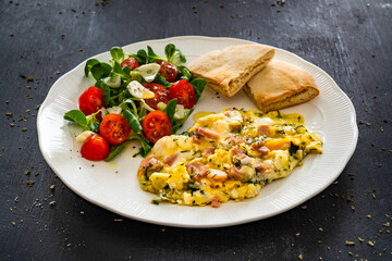 Continental breakfast - scrambled eggs with boiled ham, pita and fresh vegetables on black table	