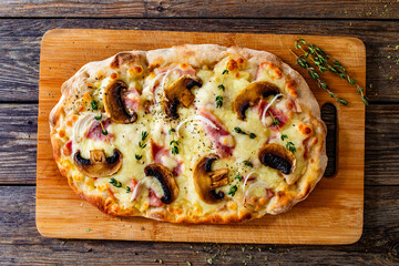 Roman Pizza with mozzarella cheese, boiled ham, onion, thyme and mushrooms on wooden table