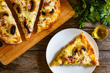 Roman Pizza with mozzarella cheese, boiled ham, onion, thyme and mushrooms on wooden table
