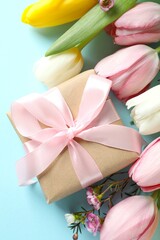 Beautiful fresh tulips with a gift box on color background