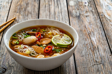 Yunnan hot pot - chinese soup with chicken meat and rice noodles on wooden table