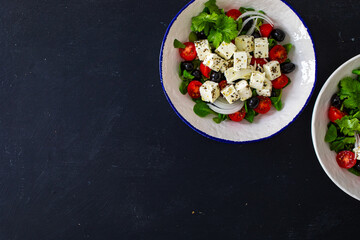 Greek style salad - fresh vegetables with feta cheese, pita bread and black olives served in bowl on black table
