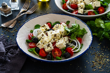 Greek style salad - fresh vegetables with feta cheese, pita bread and black olives served in bowl on black table