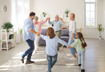 Three happy generations family common funny dance at home in new living room, congratulating, grandparent grandkid enjoying leisure time together, holiday gathering to play on special pleasant day 
