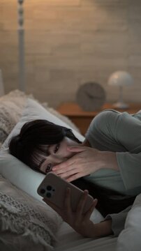 夜中にスマホを見て睡眠が足りず寝不足になってしまう女性のクローズアップでタップする動画　ニュートラルなカラー