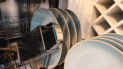 Open dishwasher with clean dishes after washing in modern white kitchen. Clean kitchen utensils in...