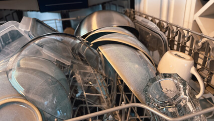 Open dishwasher with clean dishes after washing in modern white kitchen. Clean kitchen utensils in...