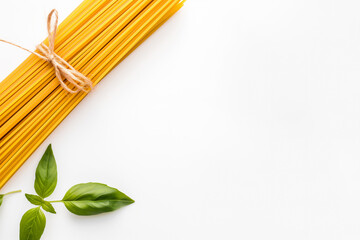A bundle of uncooked spaghetti tied with rustic twine, placed on a white background alongside fresh green basil leaves, creating a fresh and organic food presentation. Copy Space 