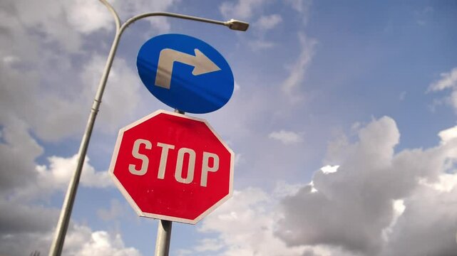 Stop sign with blue directional arrow against cloudy sky, perfect for road safety campaigns, driver education materials, traffic regulation content and urban infrastructure presentations