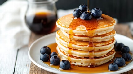 Pouring maple syrup on stack of pancakes with blueberries