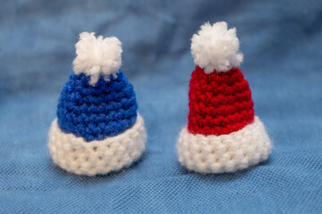 Knitted caps of blue and red color with pom-poms for a soft toy on a blue background.