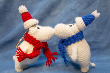 Hand-knitted soft toys, animals in a New Year's blue and red hat, stand with their noses facing each other.