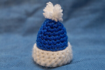 A blue cap with a white pompom for a soft toy, hand-knitted, stands on a blue background.