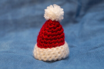 A red cap with a white pompom for a soft toy, hand-knitted, stands on a blue background.