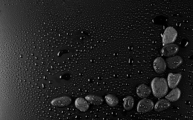 Oval stones with water drops on black background, top view