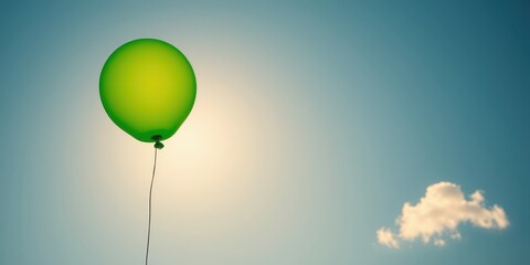 Obraz premium A single lime green balloon ascends into a vibrant, clear sky, a small cloud visible in the distance, suggesting hope and freedom.