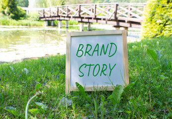 Brand Story symbol. White Blackboard with words Brand Story. Beautiful meadow background with...