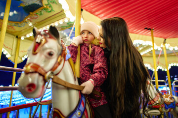 Joyful mother and daughter share a moment on a carousel at night