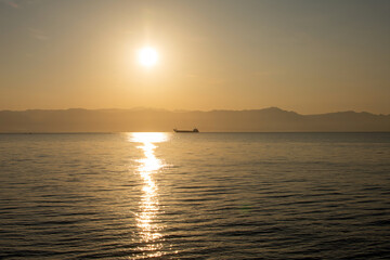 Fototapeta premium a cargo barge ferry floats at dawn on the sea against the backdrop of mountains and the rising sun, cargo and passenger transportation