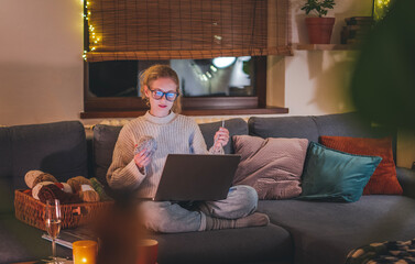 Young beautiful blonde woman with glasses learning to knit online sitting at home during Christmas...