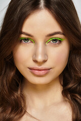 Obraz premium Young woman showcases bold beauty with striking green eyeshadow against a grey backdrop.