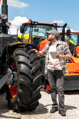 Caucasian man with digital tablet standing outdoors next to construction and agricultural machinery...