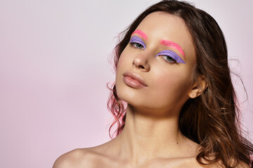Young woman displays creativity with bold makeup and vibrant colors on a grey backdrop.