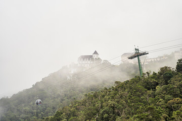 A serene view of a majestic mountain in soft mist, with a cable car station prominently in the foreground © Dima Anikin