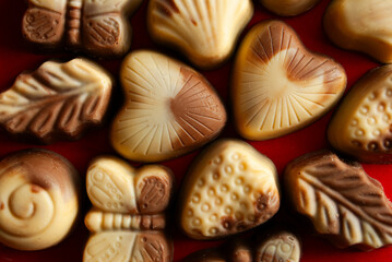 White and black chocolate pralines in various shapes, placed on a red background.