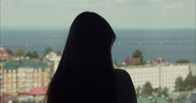 Silhouette of young woman playing with hair in front of cityscape view
