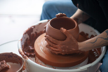 Female hands throwing a large sized bowl on a potter's wheel in a sunlit pottery studio
