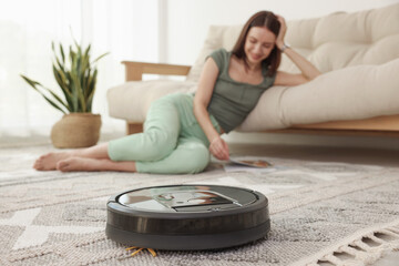 Young woman resting at home, focus on robotic vacuum cleaner